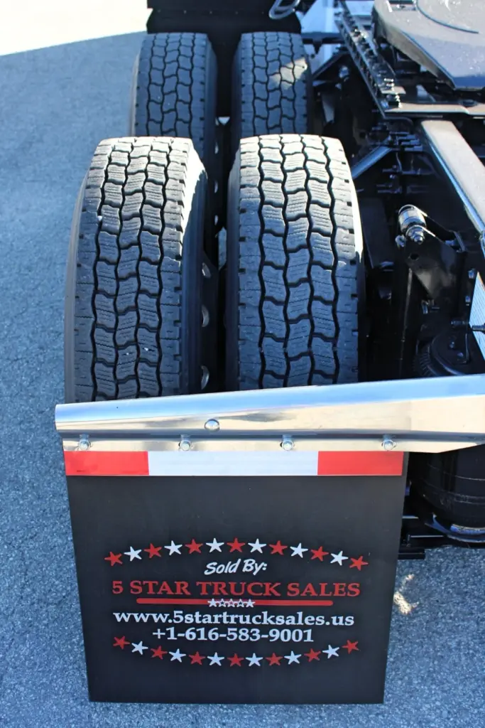 2023 Mack Anthem — close-up of dual drive tires with deep tread, stainless fender bracket and black mud flap beside the frame