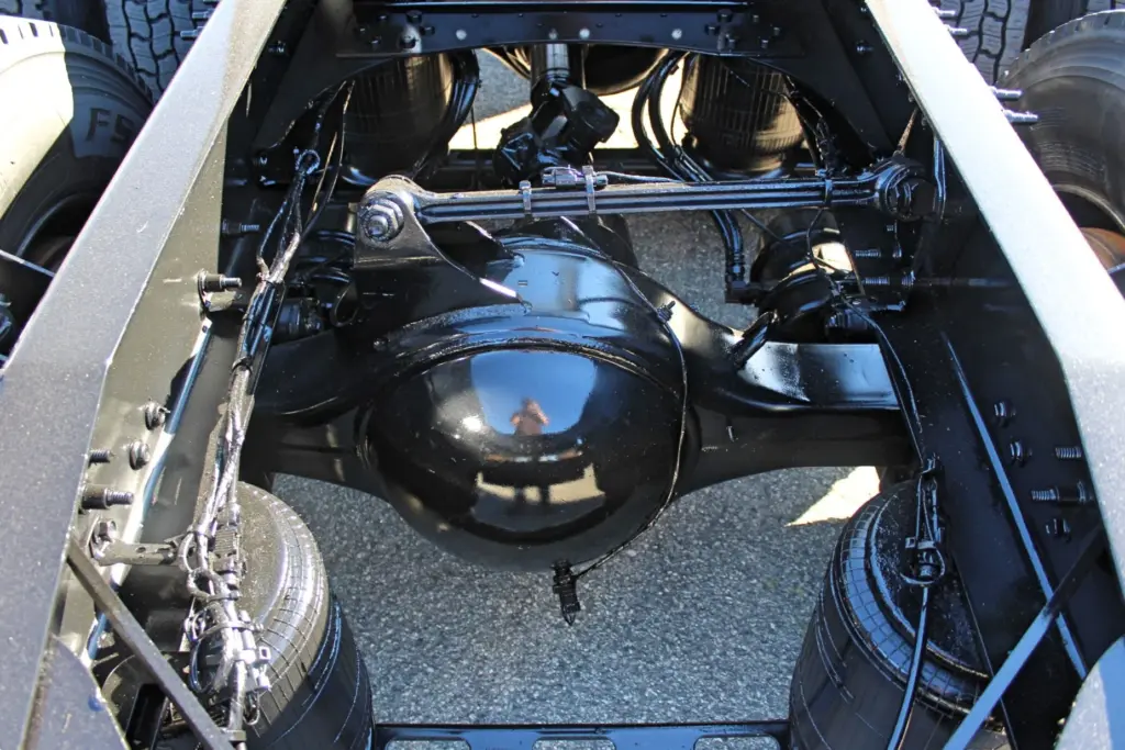 2023 Mack Anthem — view between frame rails of glossy black rear axle housing, air springs, torque rod and wiring on pavement