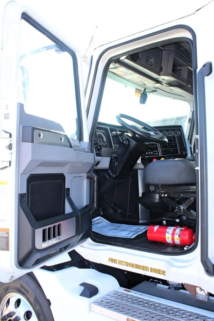 2023 Mack Anthem — open driver door showing black steering wheel, gauge cluster, gray seat, red fire extinguisher and diamond-plate step
