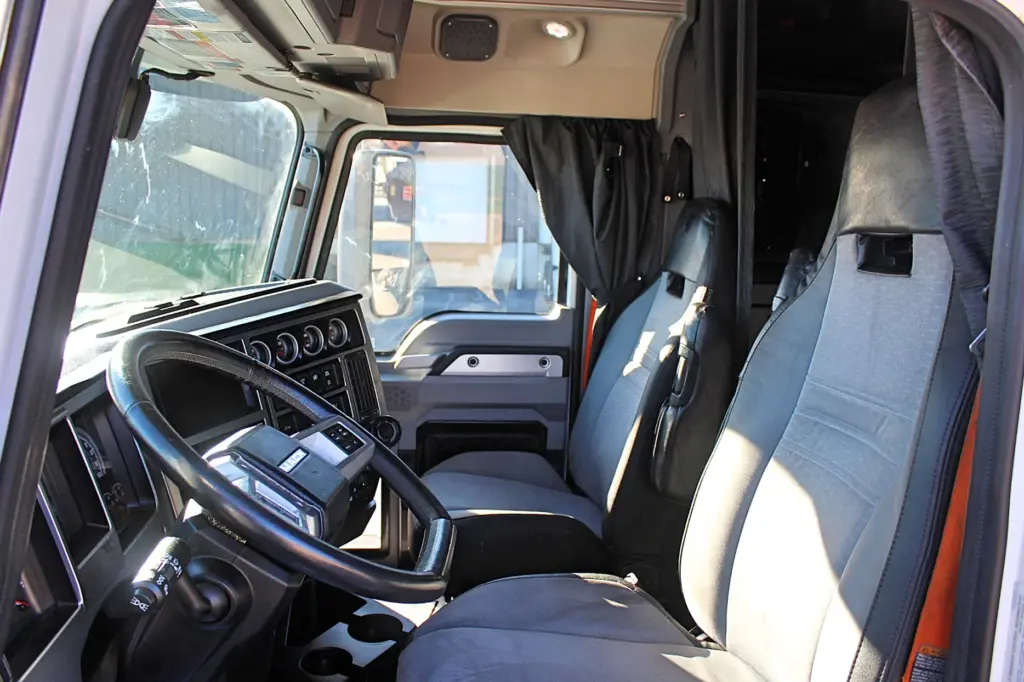 2023 Mack Anthem — cab interior with gray cloth seats, black steering wheel, dash gauges and dark privacy curtain by sleeper