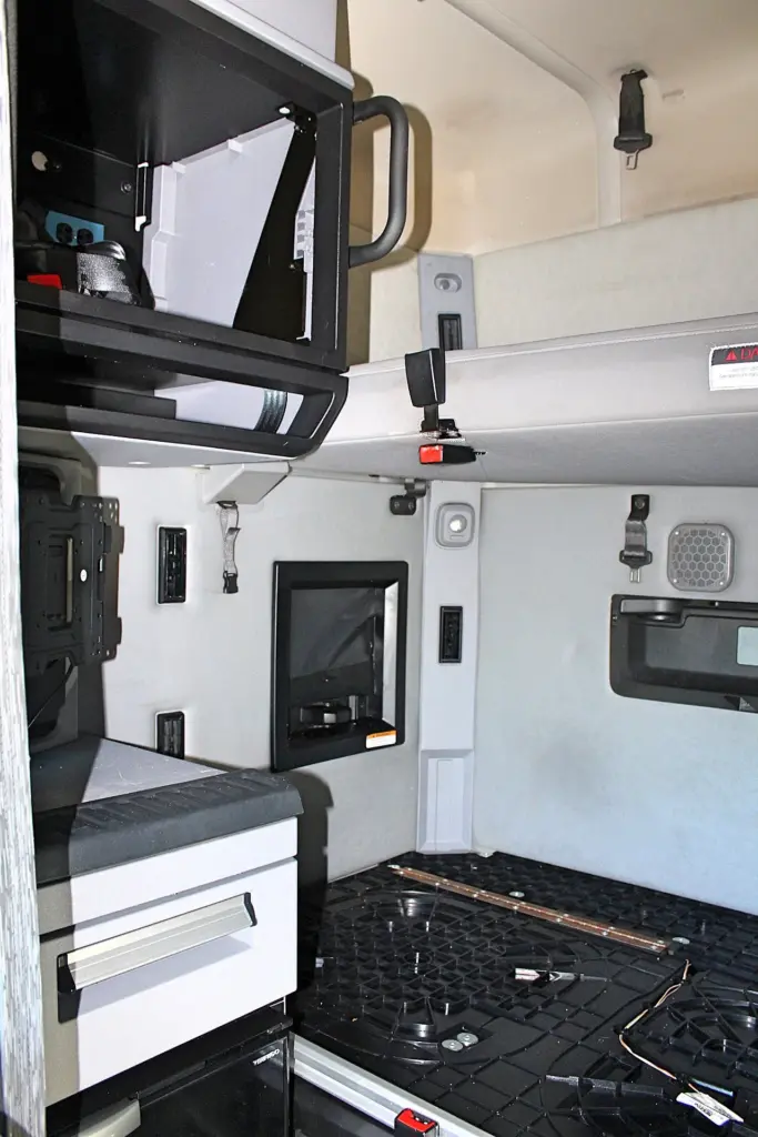 2023 Mack Anthem — sleeper interior with overhead cabinet, wall niche, upper bunk, white drawer unit and black rubber floor mat