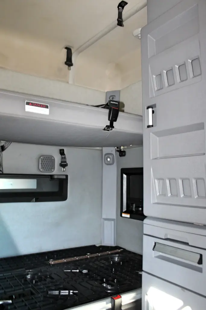 2023 Mack Anthem — upper bunk with seat belt straps, speaker, recessed TV niche, gray cabinets and black floor grid in sleeper