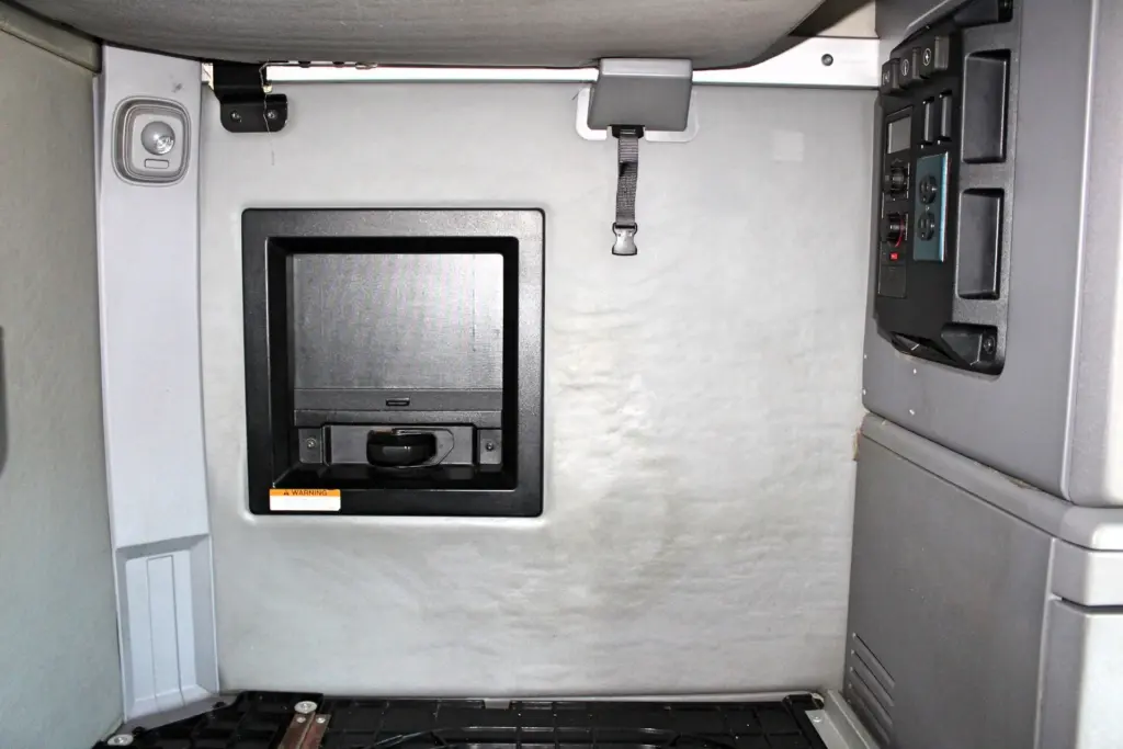 2023 Mack Anthem — sleeper wall with black recessed TV niche, warning label, gray strap, control switch panel and storage cabinets