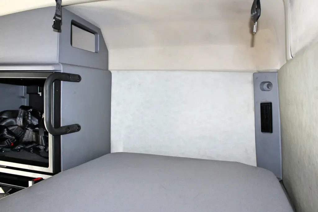 2023 Mack Anthem — sleeper bunk with gray mattress, cream padded back wall, black grab handle, restraint straps and side switch panel