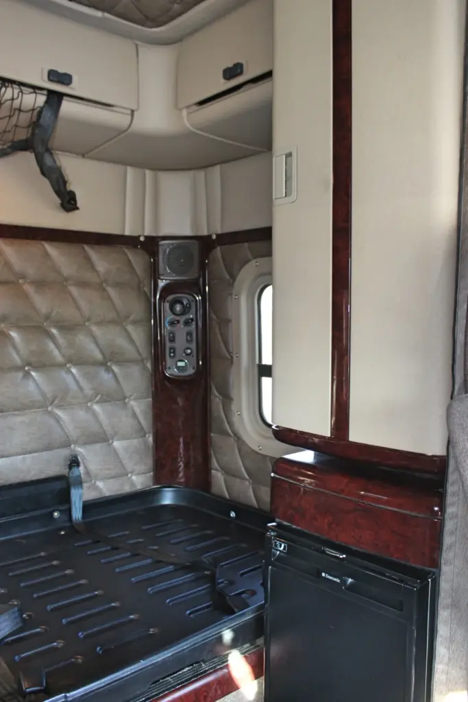 2016 Freightliner Coronado 132 — corner of sleeper with quilted tan wall, switch panel and small black fridge on wood trim