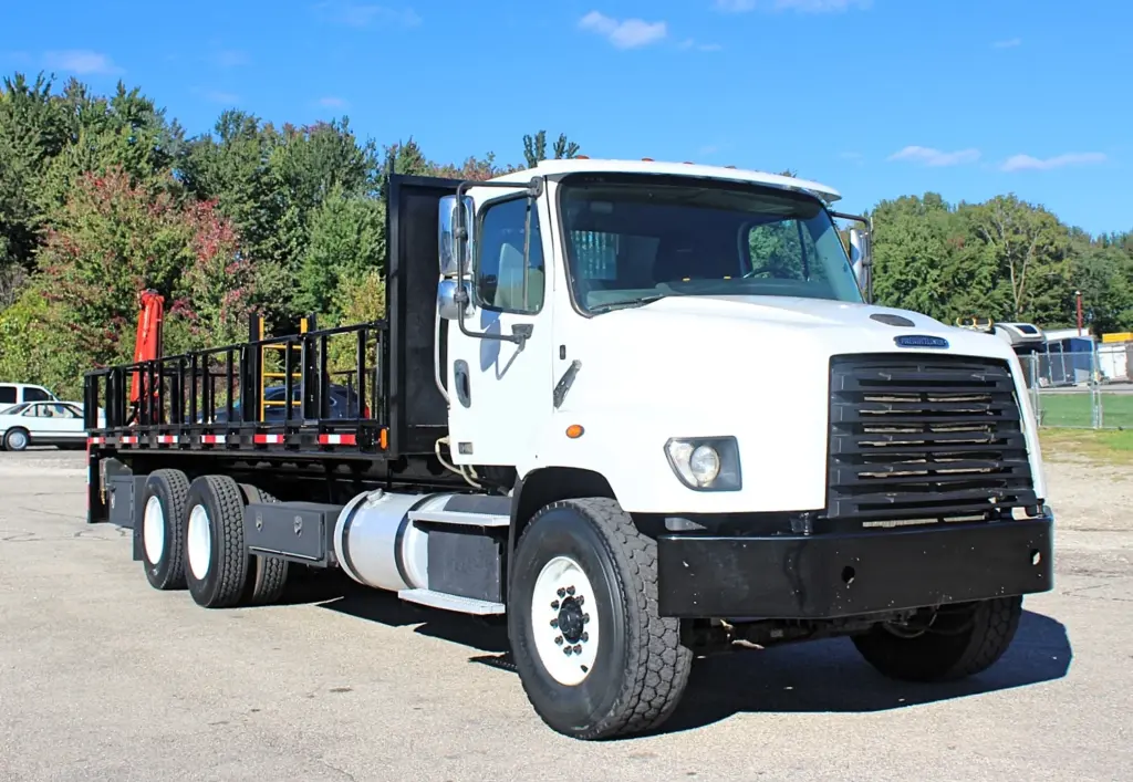 2018 Freightliner 114SD – white tandem axle flatbed crane truck with stake sides and rear-mounted knuckle boom crane.