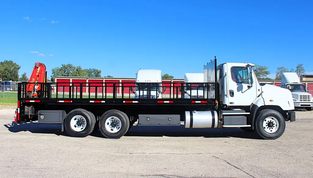 2018 Freightliner 114SD – passenger-side profile of tandem axle flatbed crane truck with stake body and hydraulic crane.
