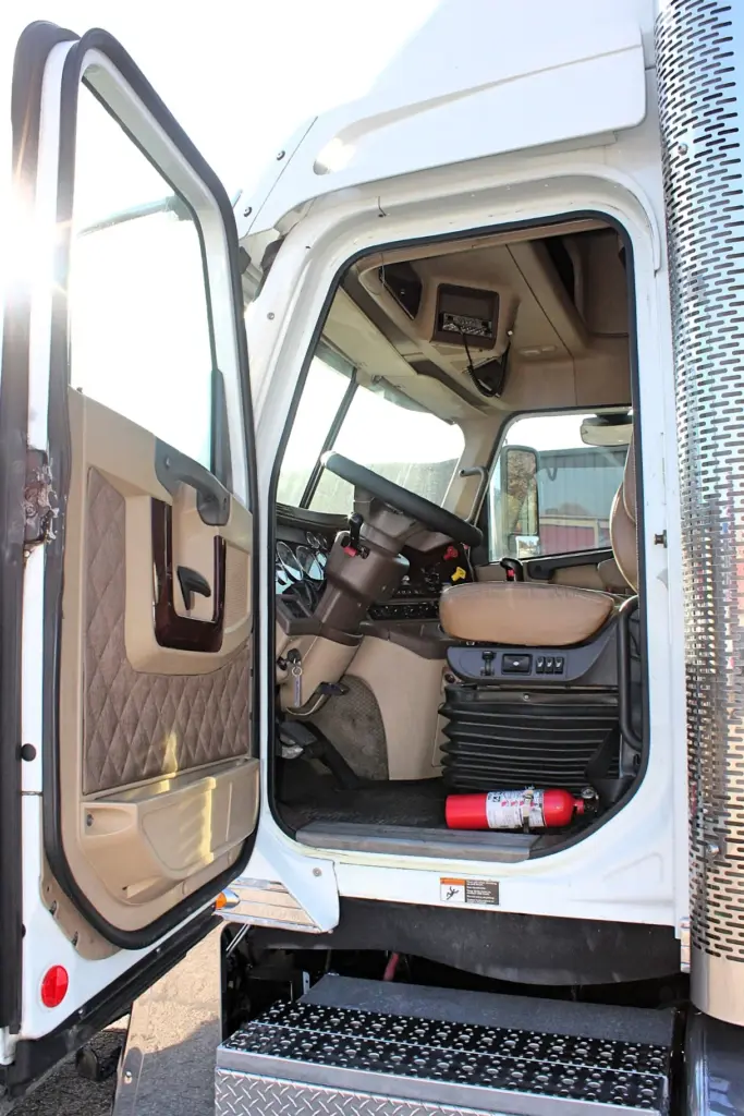2018 Freightliner Coronado 132 — open driver door showing tan quilted panel, steering wheel and red fire extinguisher in cab