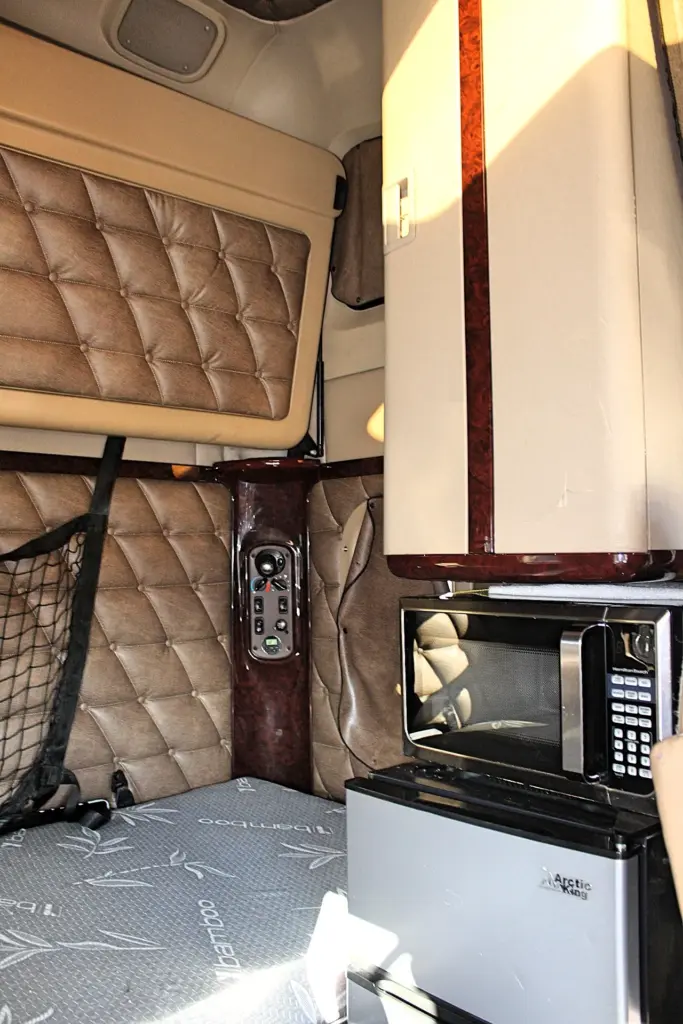 2018 Freightliner Coronado 132 — close view of sleeper with microwave on mini fridge beside wood-trim control panel