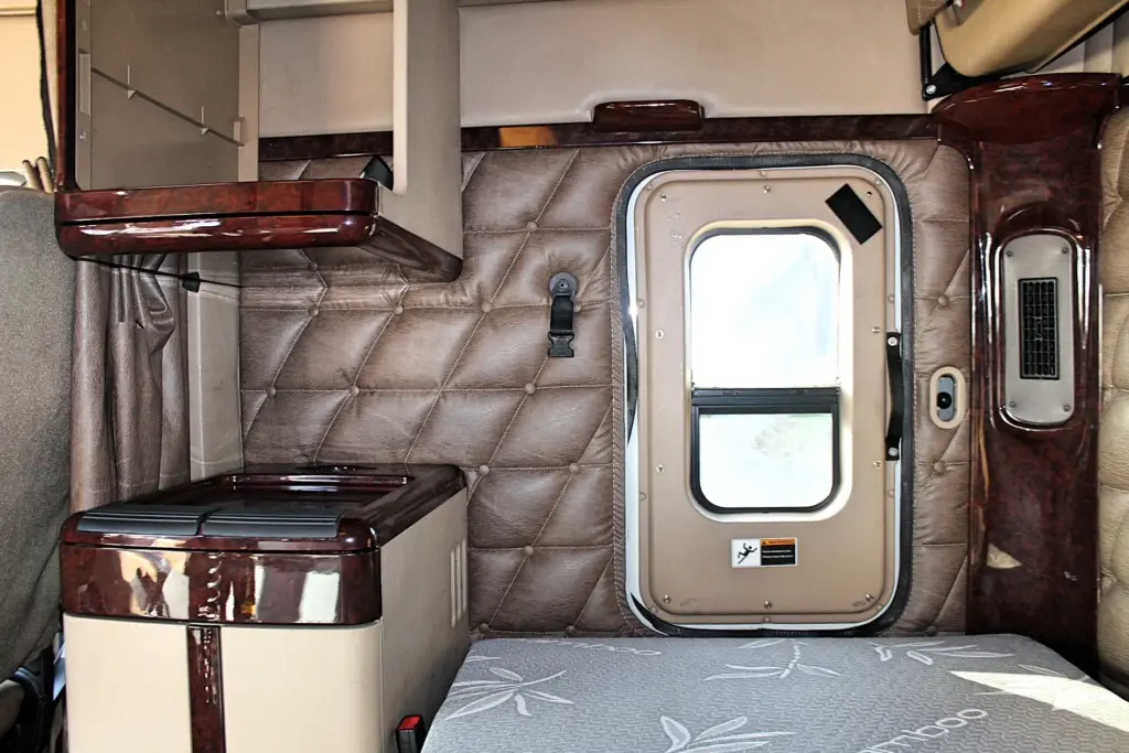 2018 Freightliner Coronado 132 — wide view of sleeper with brown diamond-quilted wall, door with window and gray mattress