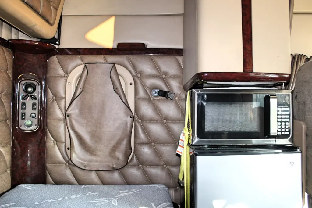 2018 Freightliner Coronado 132 — angled view of microwave atop silver fridge beside tufted brown wall and hatch cover.