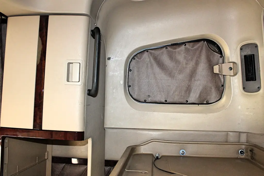 2018 Freightliner Coronado 132 — angled sleeper wall with gray fabric hatch, black grab handle and cream wood-trim panel