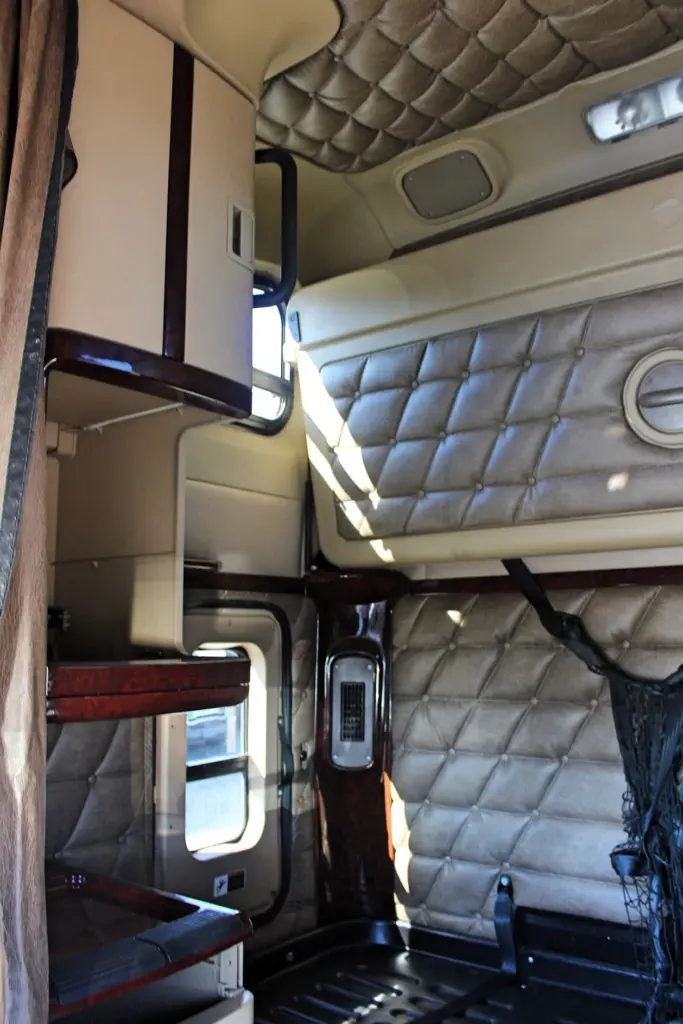2020 Freightliner Coronado 132 — angled view of sleeper bunk with quilted tan walls, wood-trim shelves and black net
