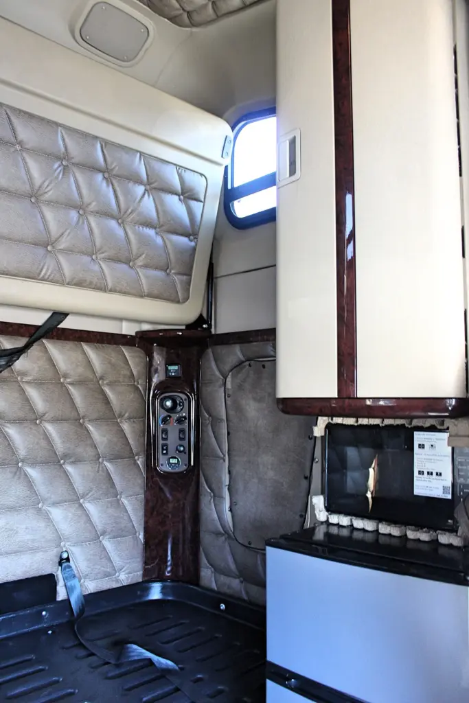 2020 Freightliner Coronado 132 — sleeper corner with quilted tan wall, wood-trim switch panel and cream overhead cabinet