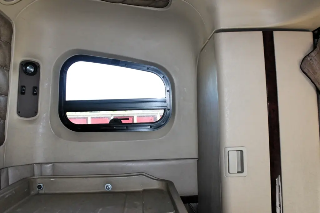 2020 Freightliner Coronado 132 — interior view of tan sleeper wall with porthole window, wood-trim edge and latch panel