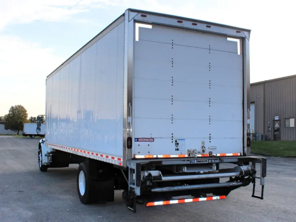 2020 Freightliner M2 106 — angled rear view of white box body with closed roll door and a lowered cargo lift platform beneath