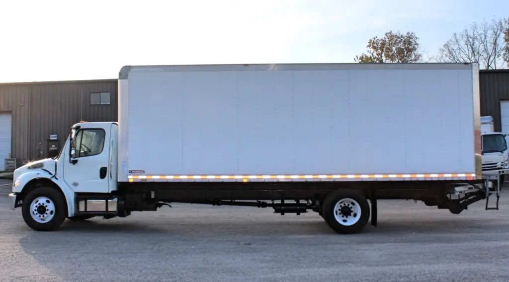 2020 Freightliner M2 106 — full-length side view of white dry box body, amber marker lights along the base, tail lift at rear