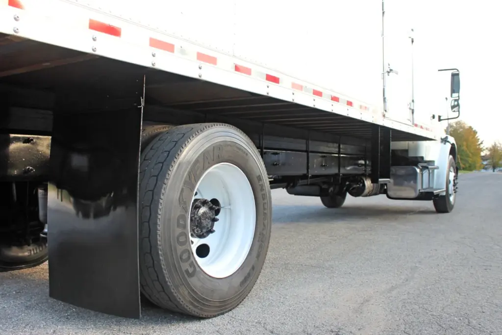 2020 Freightliner M2 106 — low-angle shot of a rear tire on white steel wheel beside black mud flap, box floor and cab beyond