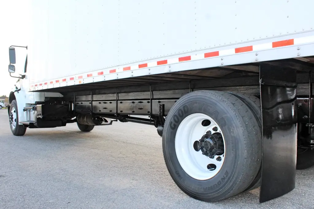 2020 Freightliner M2 106 — ground-level side view of dual rear tires under the box, with red-and-white reflective trim above