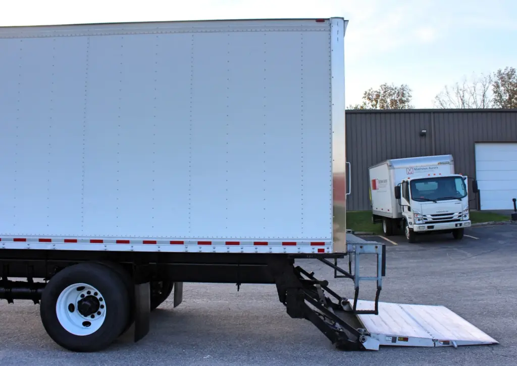2020 Freightliner M2 106 — side view of white box body with lowered tail lift extended to the pavement and rear wheel
