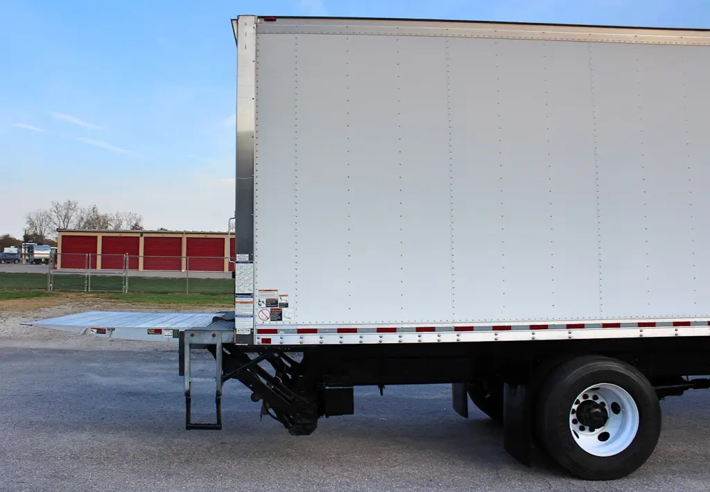 2020 Freightliner M2 106 — rear three-quarter view of white box body, tail lift lowered toward pavement by rear tire