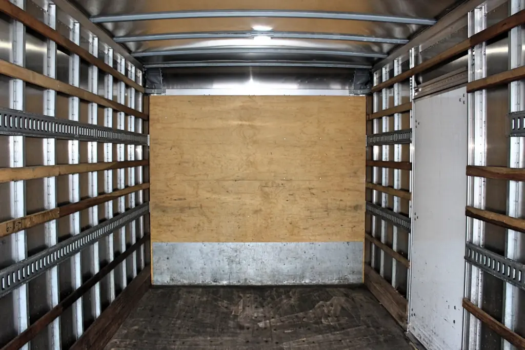 2020 Freightliner M2 106 — forward view inside the empty box, plywood bulkhead, lit ceiling and side door on the right
