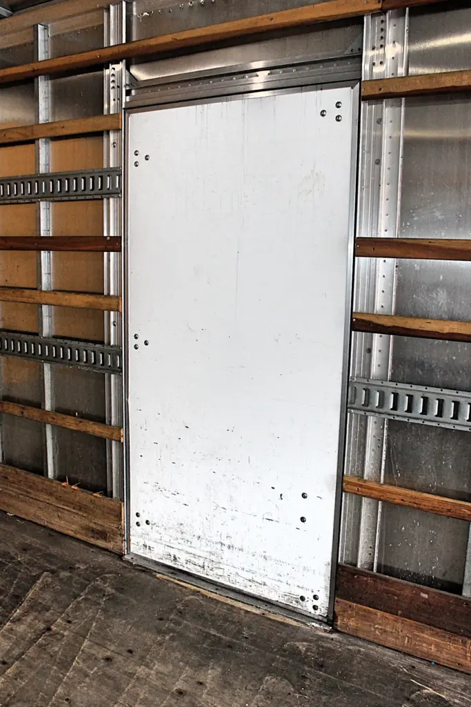 2020 Freightliner M2 106 — closed aluminum door panel framed by wood slats and steel tie rails inside the box, scuffed floor