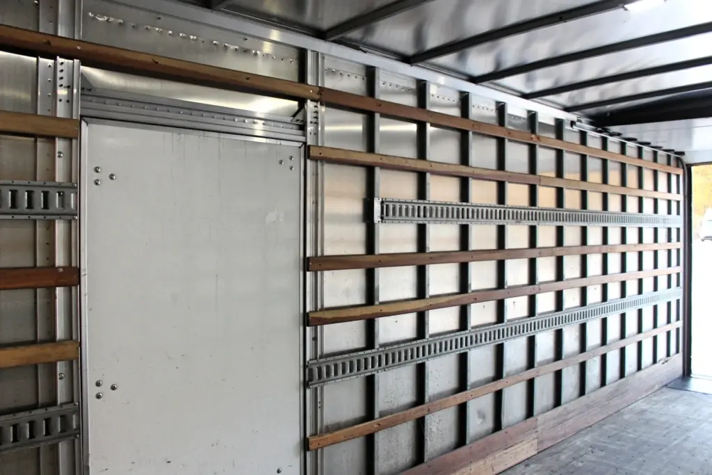 2020 Freightliner M2 106 — inside box facing rear doorway, closed side door beside wood rails and steel tie rails