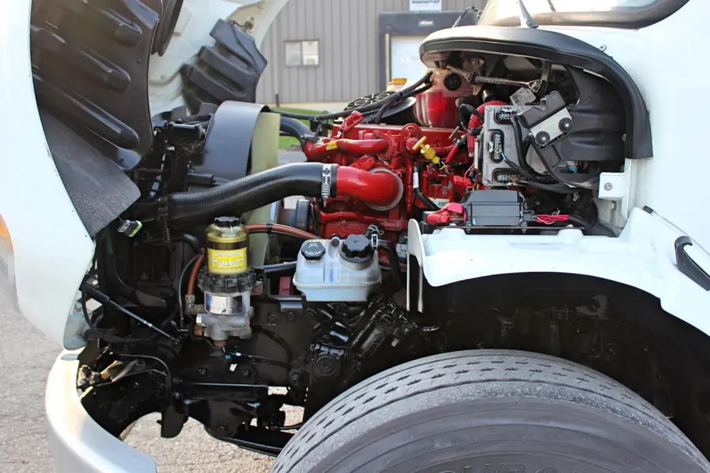 2020 Freightliner M2 106 — close-up into open hood showing red Cummins B6.7L engine, yellow steering reservoir and front tire