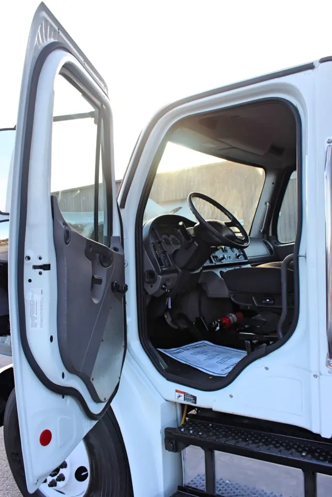 2020 Freightliner M2 106 — open driver door revealing black steering wheel, gauge cluster and dash in the cab interior