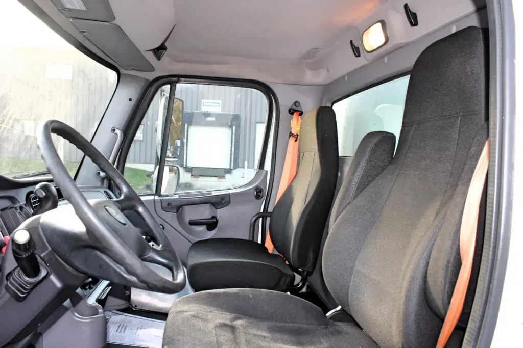 2020 Freightliner M2 106 — driver seat and black steering wheel in cab interior with orange seatbelt and gray dash trim