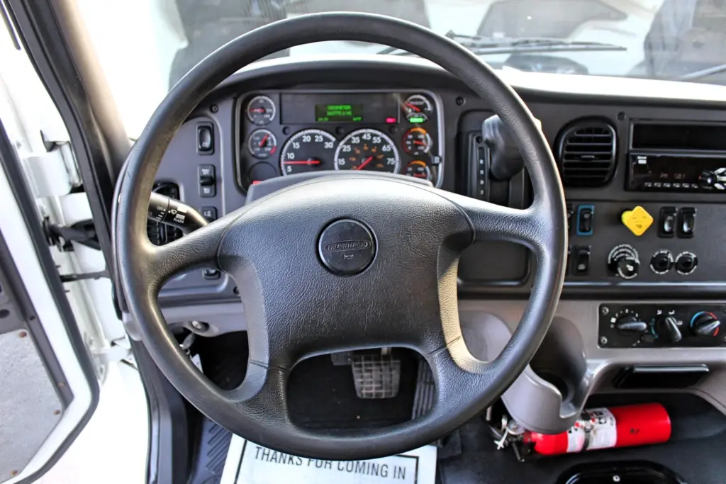 2020 Freightliner M2 106 — driver-side view of steering wheel, gauge cluster and dash with red fire extinguisher on floor