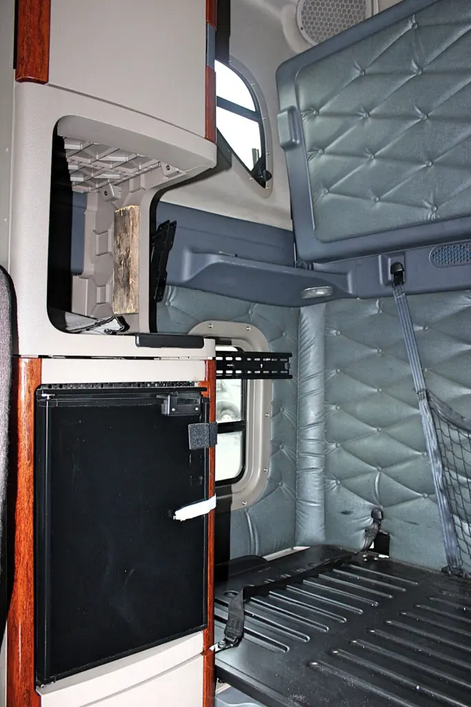2020 Freightliner Cascadia 125 Glider – sleeper interior with bunk, storage cabinets and woodgrain trim.