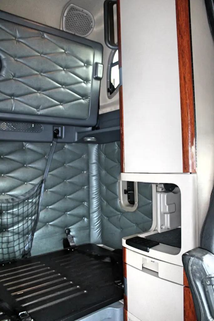 2020 Freightliner Cascadia 125 Glider – sleeper compartment with bunk, storage cabinet and woodgrain interior trim.