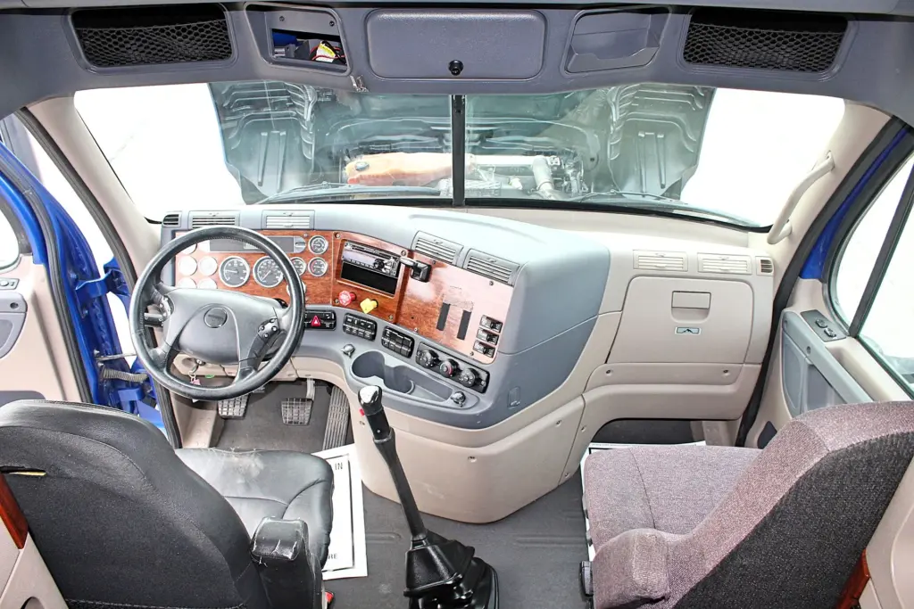 2020 Freightliner Cascadia 125 Glider – wide cab interior view showing woodgrain dashboard, seats and manual shifter.