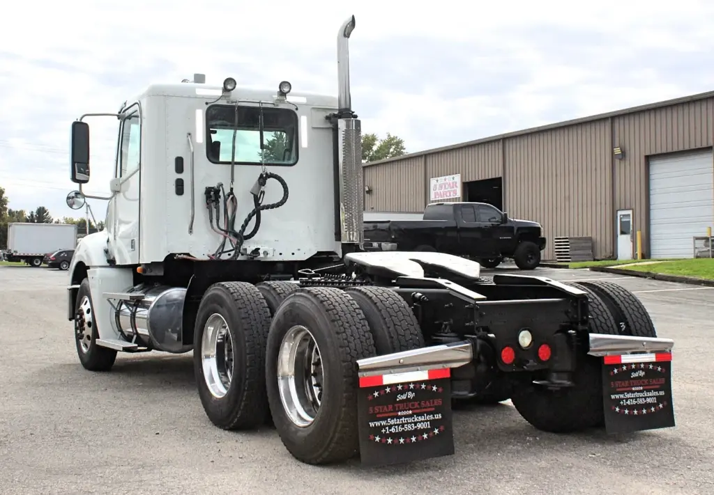2020 Freightliner Columbia 120 — angled back view of white day cab with polished aluminum wheels and tall exhaust stack.