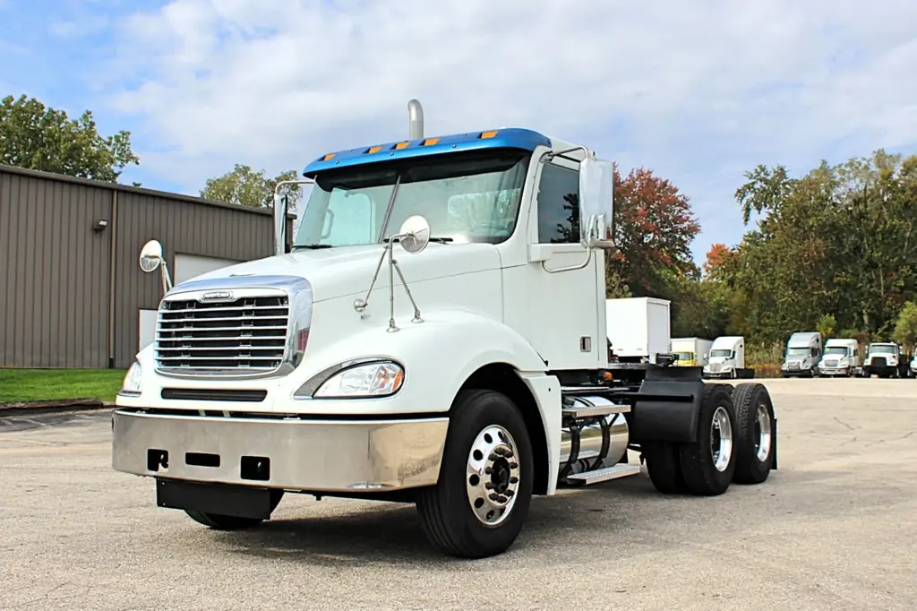 2020 Freightliner Columbia 120 — angled front view of white tractor with blue roof fairing and chrome bumper.