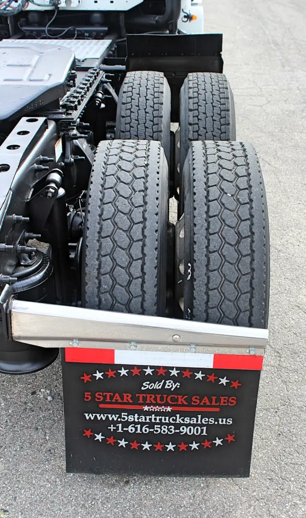 2020 Freightliner Columbia 120 — rear-facing view of tandem drive tires, chrome mud flap bar and black lower chassis frame.