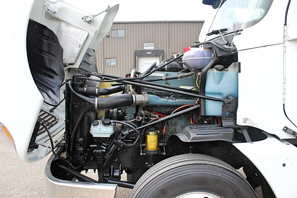 2020 Freightliner Columbia 120 — side angle of engine bay under raised hood with black intake hose and yellow fuel filter.