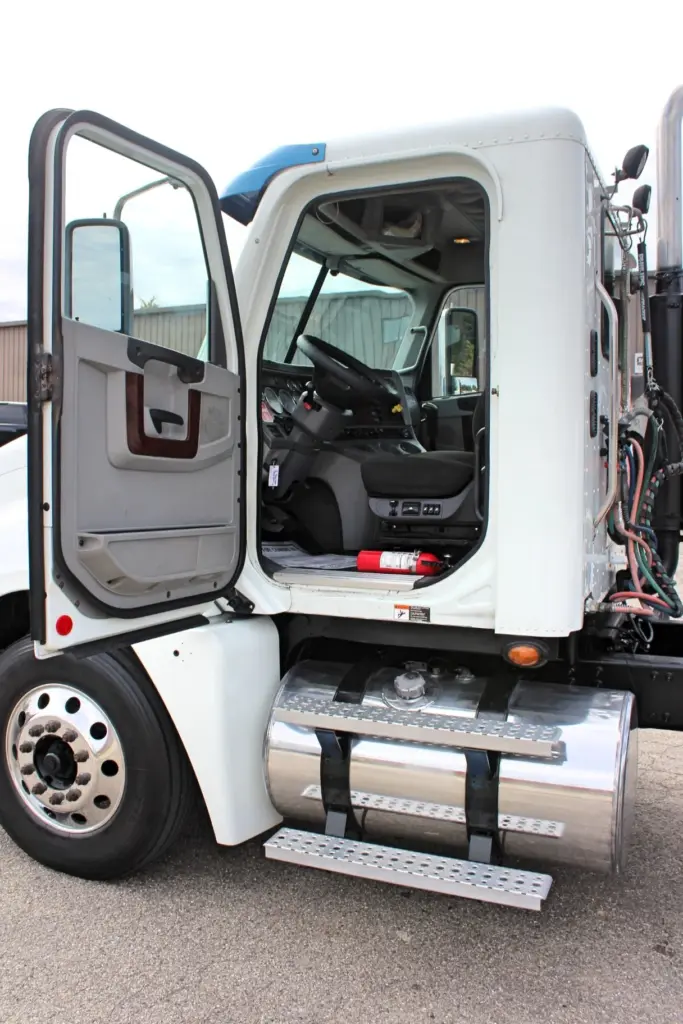 2020 Freightliner Columbia 120 — open driver door reveals white dash, steering wheel and red fire extinguisher on floor.