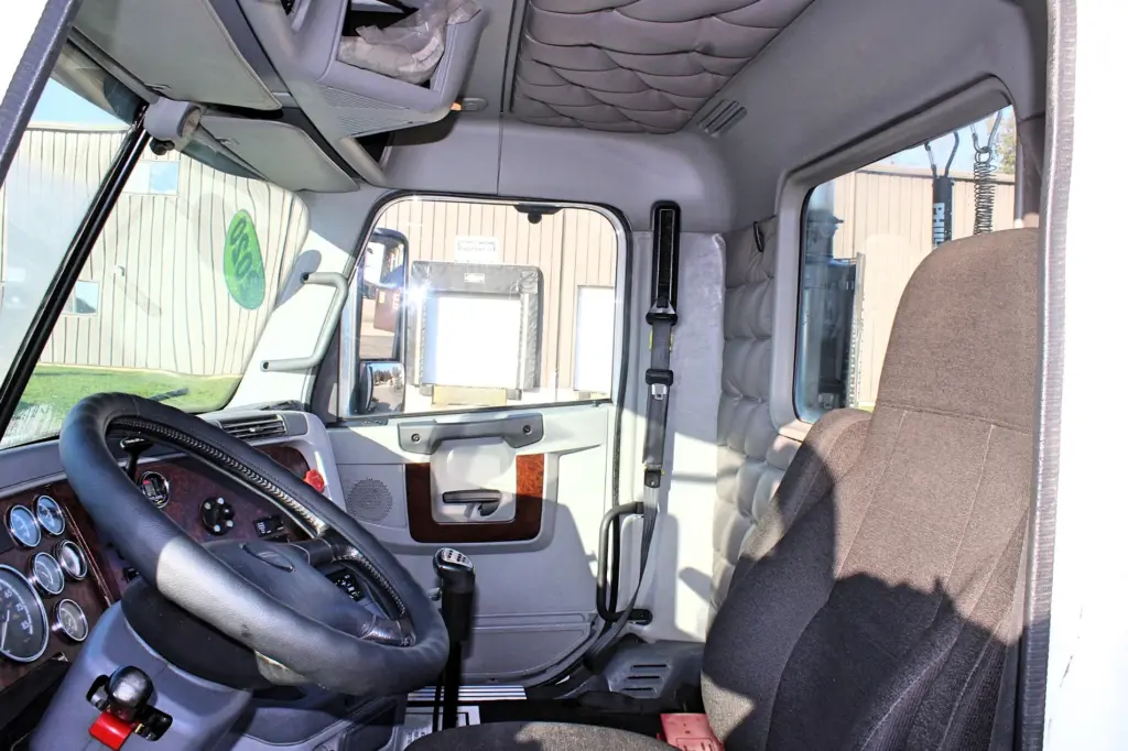 2020 Freightliner Columbia 120 — interior shot across cab of black steering wheel, gauges and gray cloth seat.