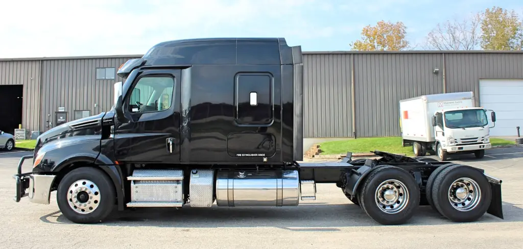 2021 Freightliner Cascadia 126 — full side view of black sleeper cab, bright aluminum wheels and tandem axles on pavement