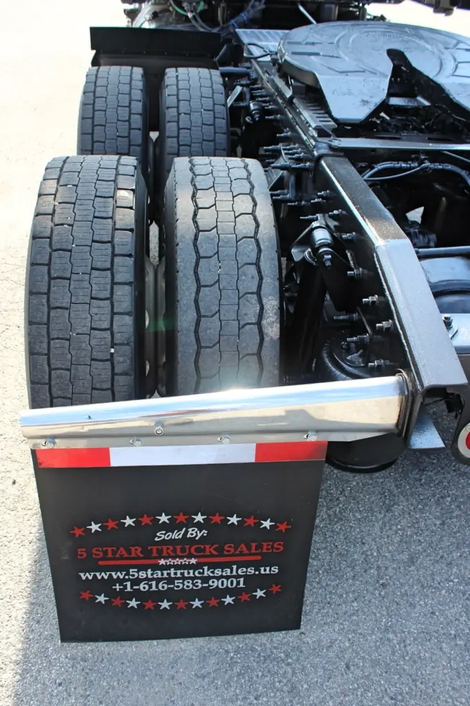 2021 Freightliner Cascadia 126 — close angled view of rear tandem tires, chrome bar and black mudflap