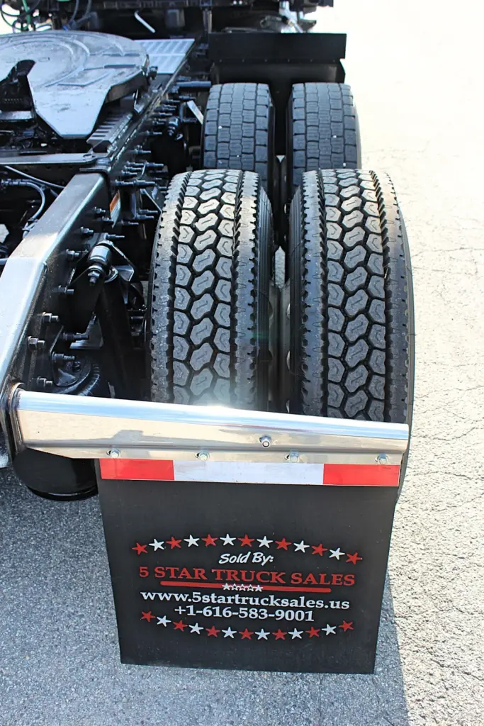 2021 Freightliner Cascadia 126 — rear view of tandem axle with dual tires and a silver bar above the black mudflap