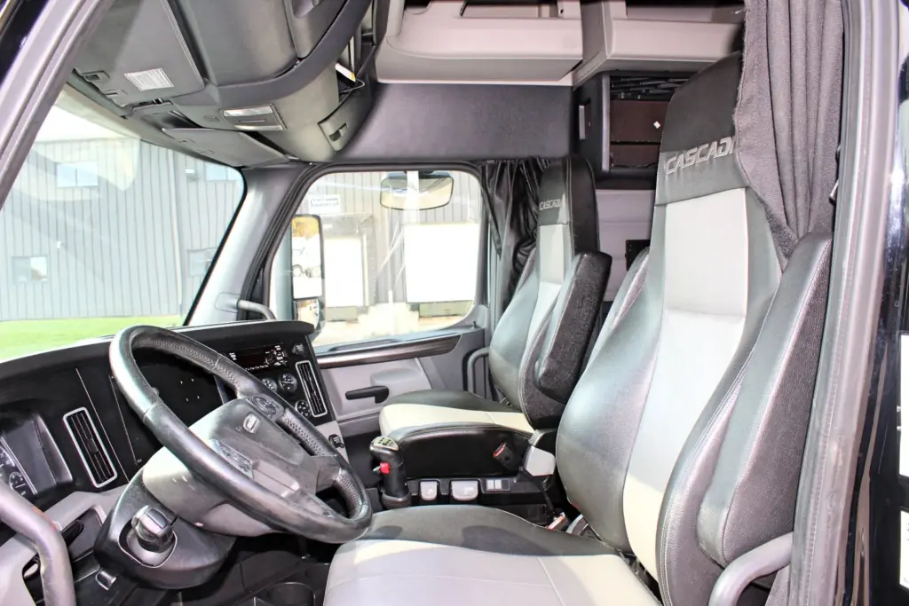 2021 Freightliner Cascadia 126 — interior view of driver seat, steering wheel and dash with two-tone gray leather seating.