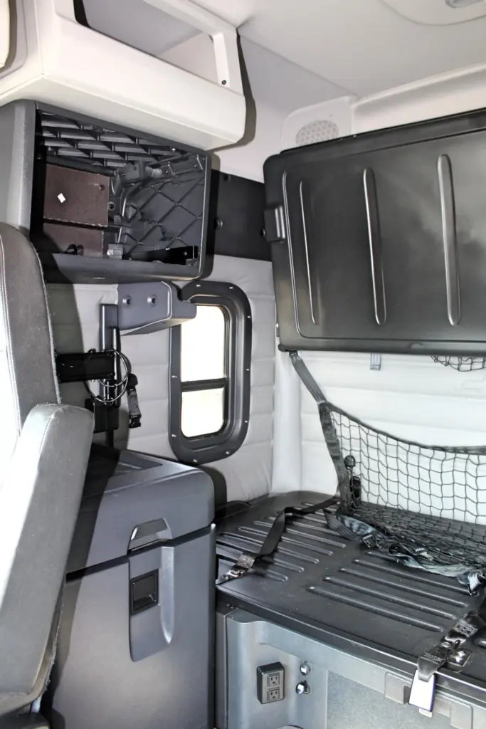 2021 Freightliner Cascadia 126 — sleeper bunk area with overhead black storage box, cargo net and round side window