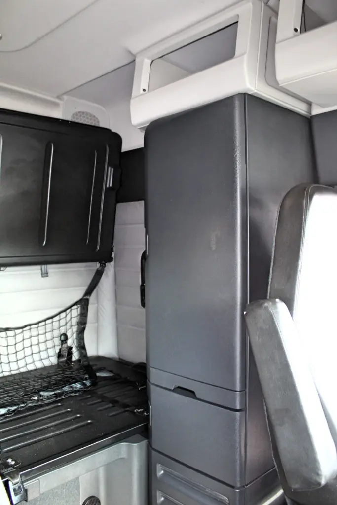 2021 Freightliner Cascadia 126 — angled view of sleeper interior with dark gray cabinet column, bunk cargo net and gray seat