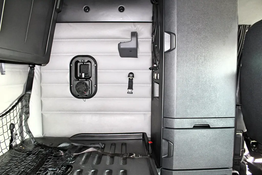 2021 Freightliner Cascadia 126 — rear wall view of gray quilted panel with black vent fan, seat belt buckle and cargo net