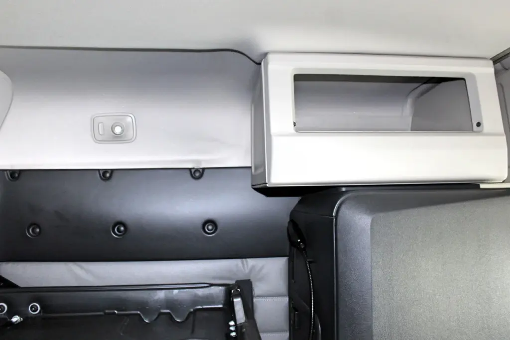 2021 Freightliner Cascadia 126 — close view of a tufted gray wall, white overhead cubby with open front, and black cabinet