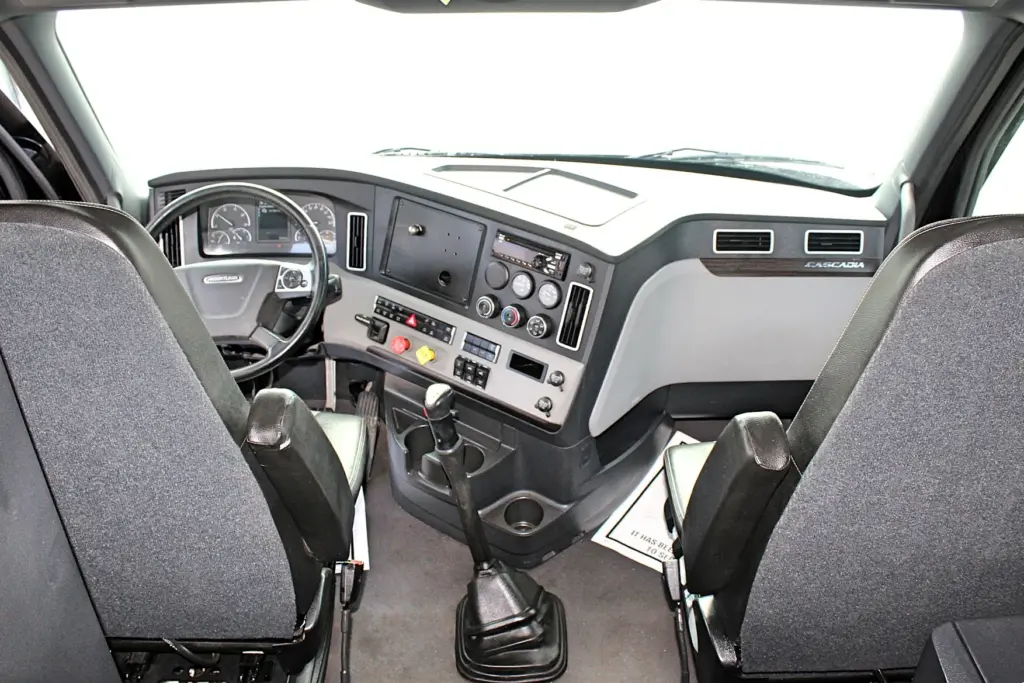 2021 Freightliner Cascadia 126 — forward view from the cab across two gray seats to the wheel, shifter and dash
